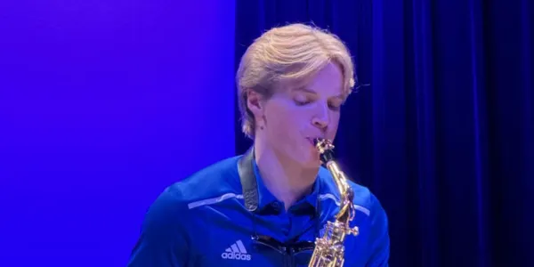 Student playing saxophone under blue stage lights