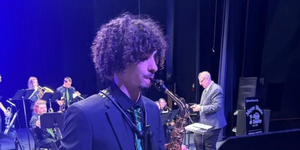 Student saxophonist performing with band on stage